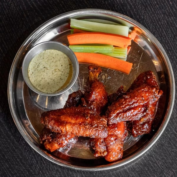 Halal chicken wings with a side of ranch, carrots, and celery on a silver platter.