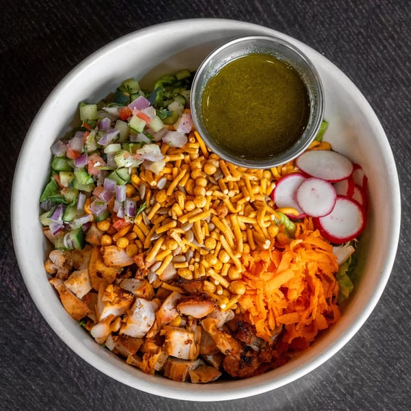 Mirchi Cafe's halal salad bowl with chicken, vegetables, crunchy toppings, and a side of dressing.