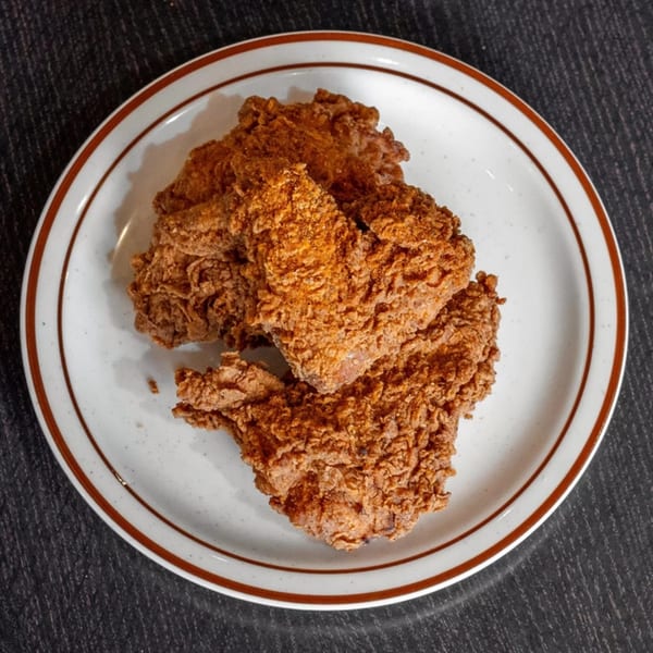Three pieces of golden-brown fried chicken with crispy breading on a white plate with a brown rim.