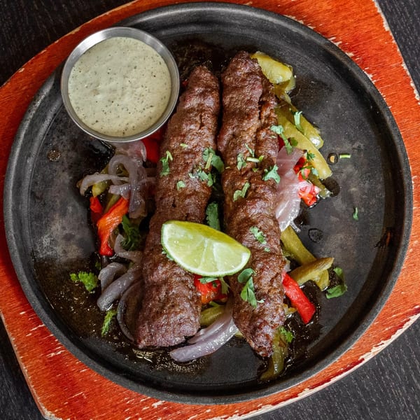 Two Mirchi Cafe seekh kebabs with grilled vegetables, lime, and a side of green sauce.