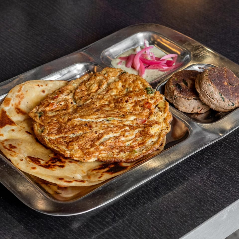 Halal breakfast platter with an omelet, flatbread, two patties, and a small dish of pickled onions.