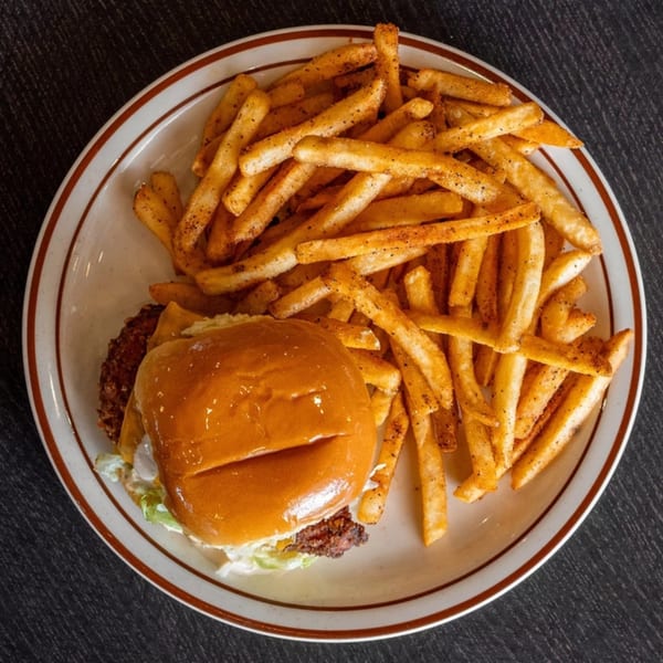 A Mirchi Cafe burger with lettuce, cheese, and a side of seasoned french fries on a white plate.