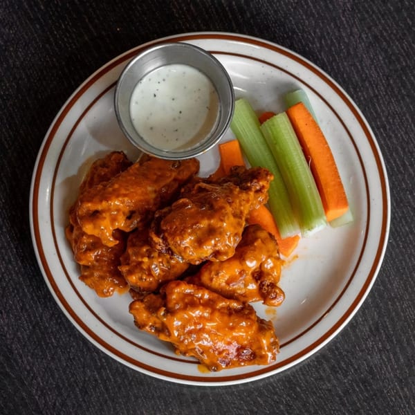 Plate of buffalo wings with ranch dressing, celery, and carrot sticks.