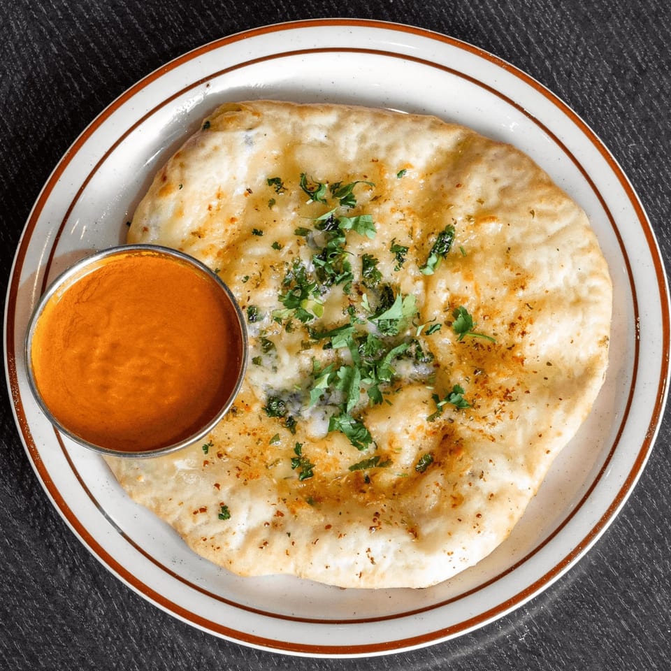 Round herb-topped flatbread served on a decorative plate with a bowl of orange dipping sauce.