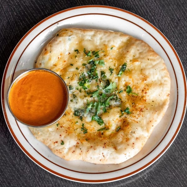 Garlic naan bread with fresh cilantro and a side of orange curry sauce on a white plate.