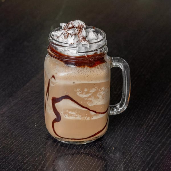 A Mirchi Cafe frappe in a mason jar, topped with whipped cream and chocolate drizzle.